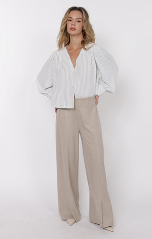 Woman wearing a white blouse with puffed sleeves and beige pants on a white background