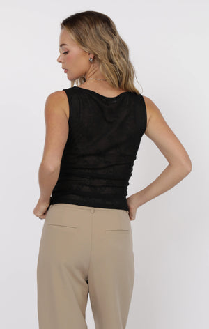 Woman wearing a black sleeveless top and beige pants on a white background