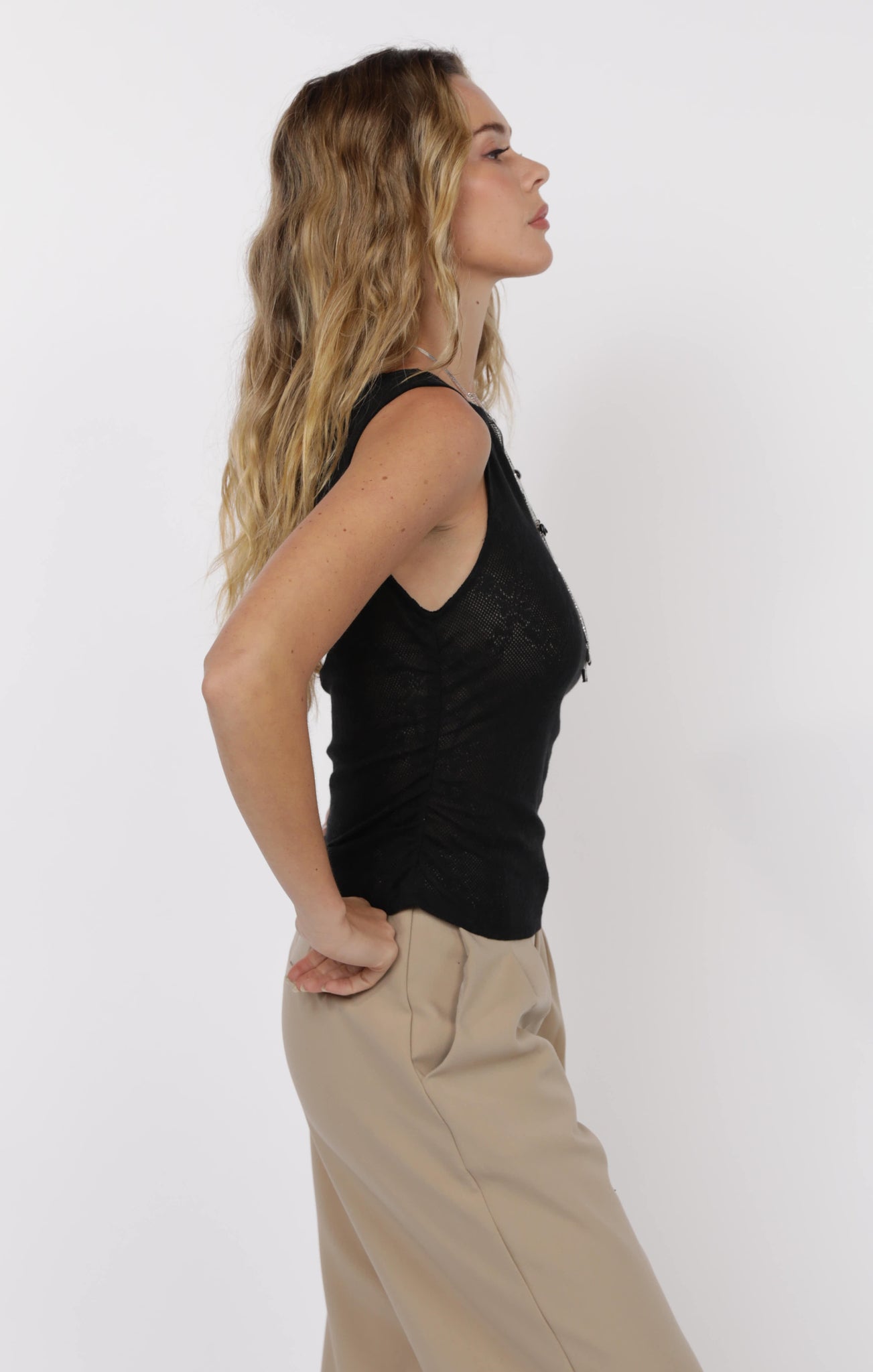 Woman wearing a black sleeveless top and beige pants on a white background