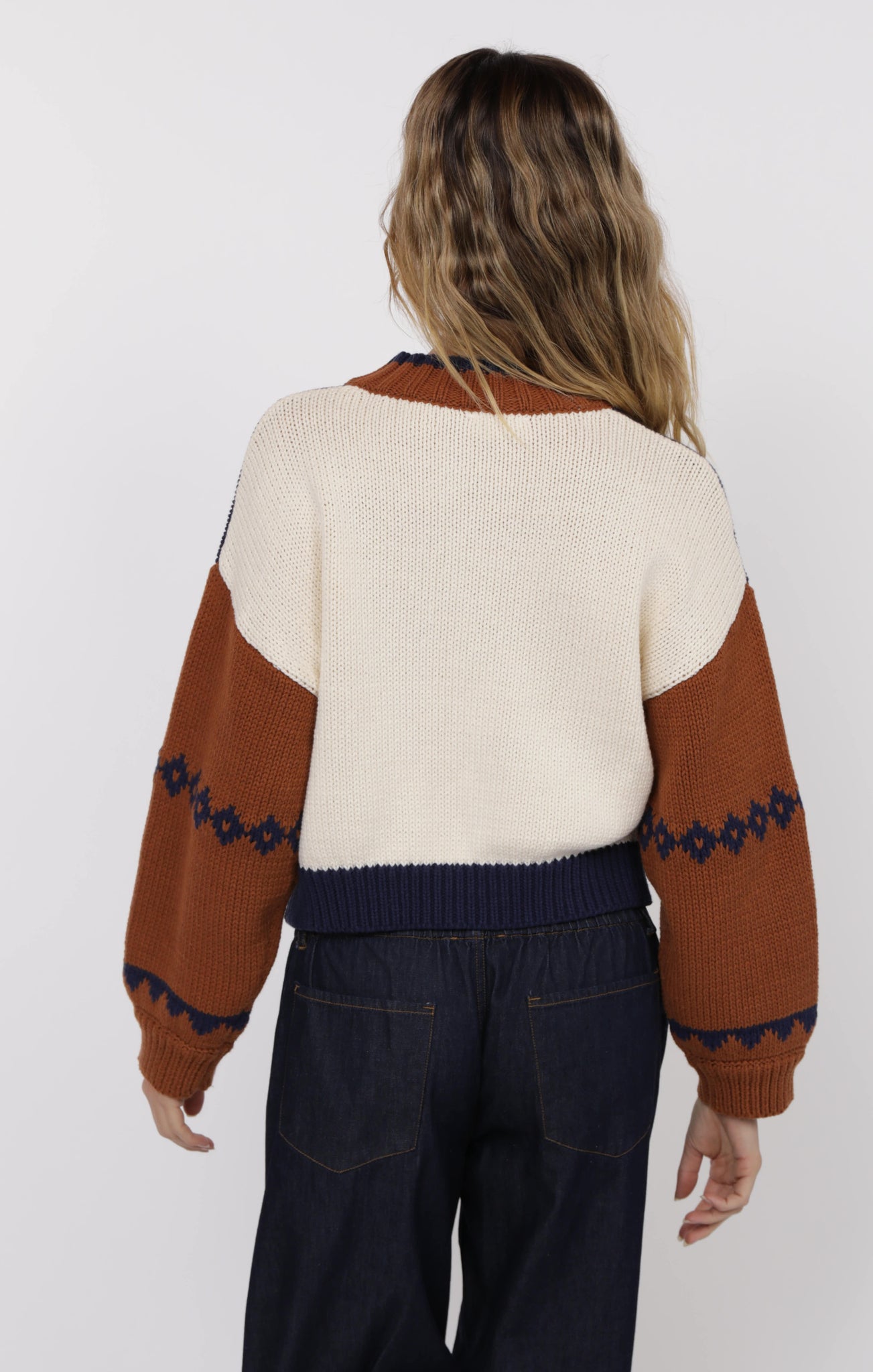 Person wearing a cream and brown sweater with blue patterns on a white background