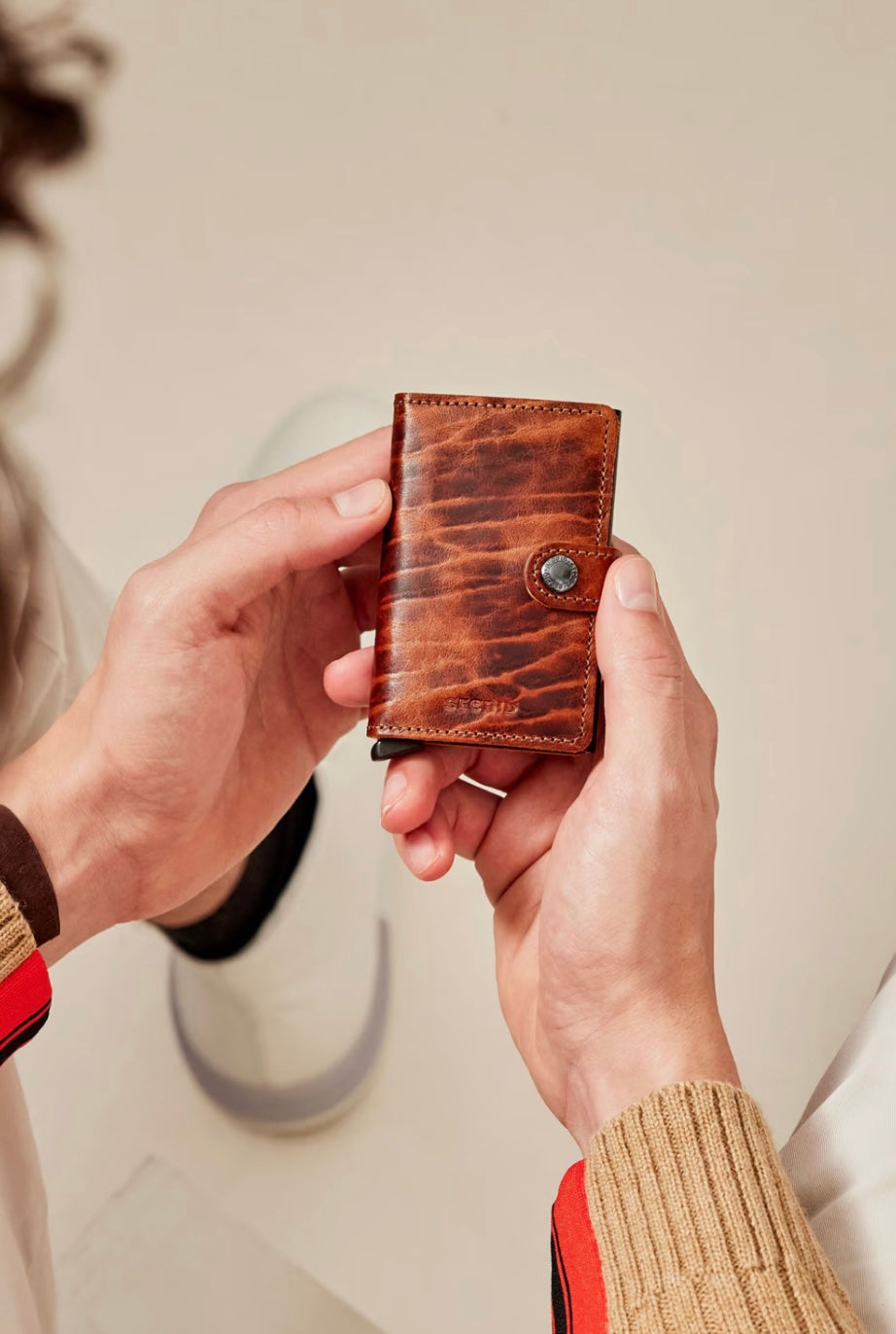 Person holding a brown leather wallet against a neutral background