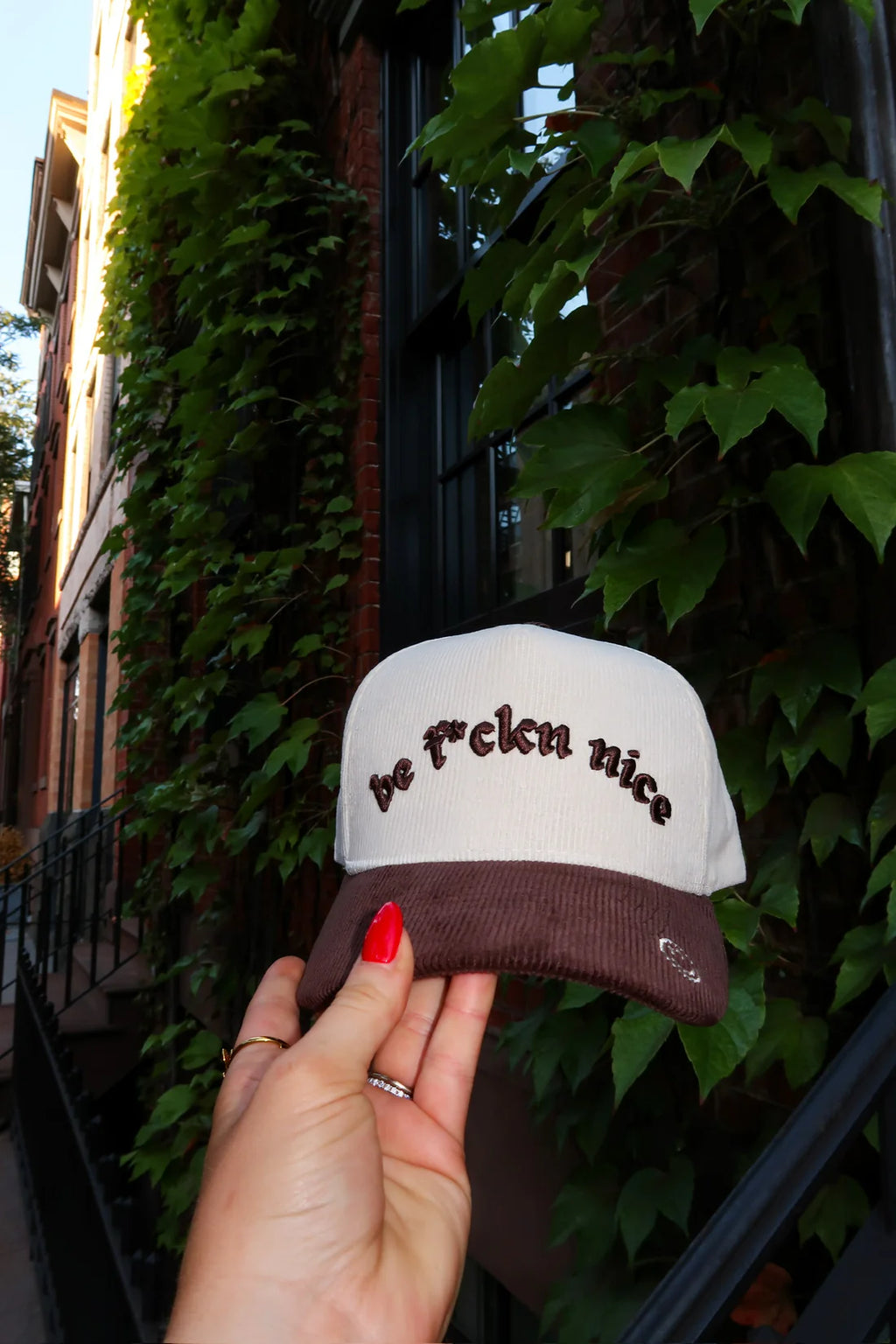 Hand holding a white cap with brown text against a leafy background
