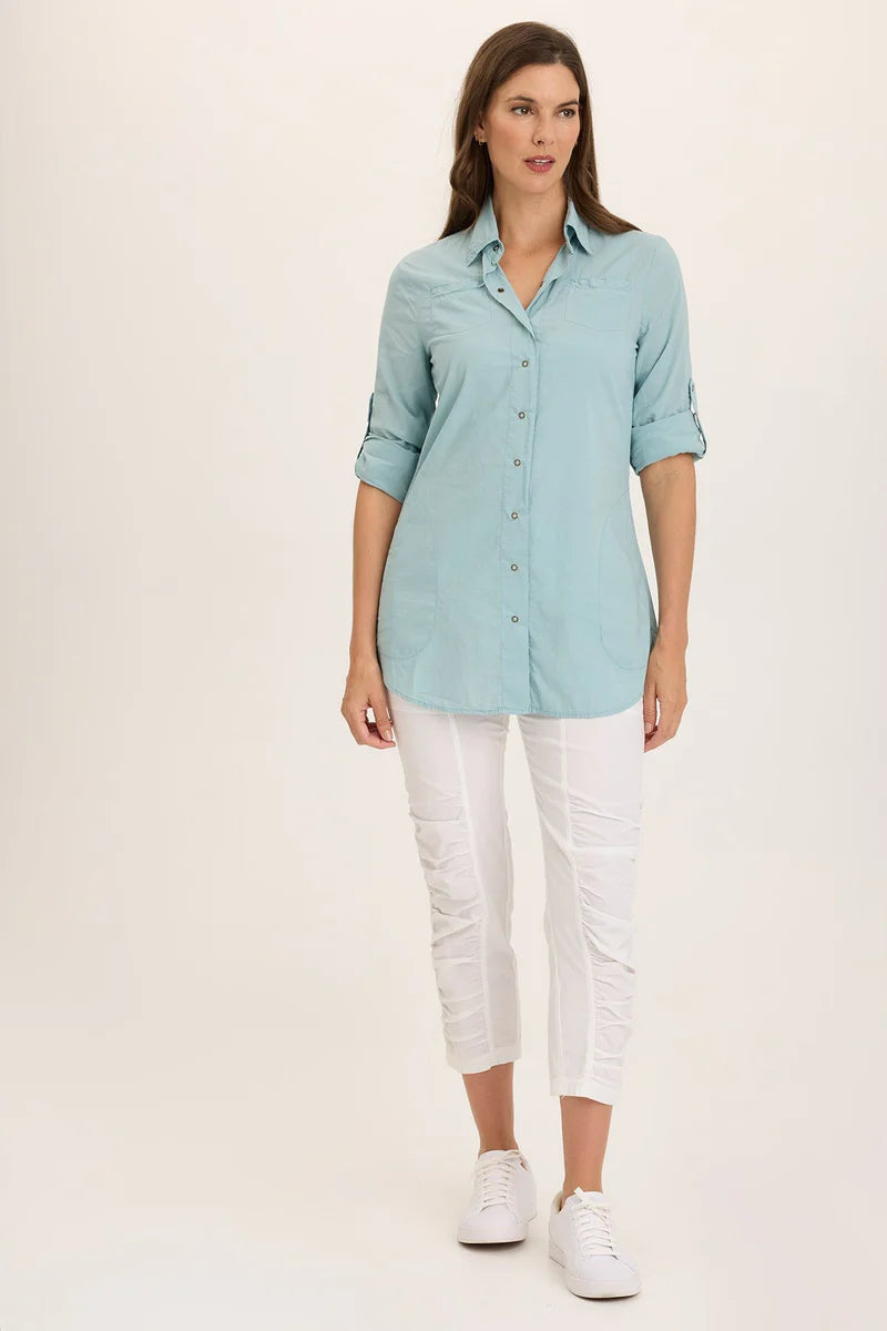 Woman wearing a light blue shirt and white pants on a plain background