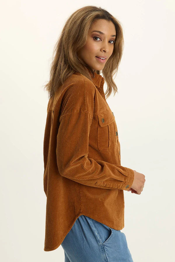 Woman wearing a brown corduroy shirt and blue jeans on a beige background