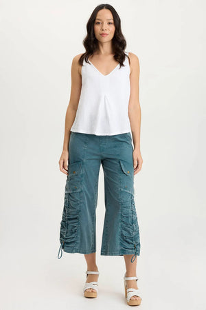 Woman wearing a white sleeveless top and teal cargo pants on a white background