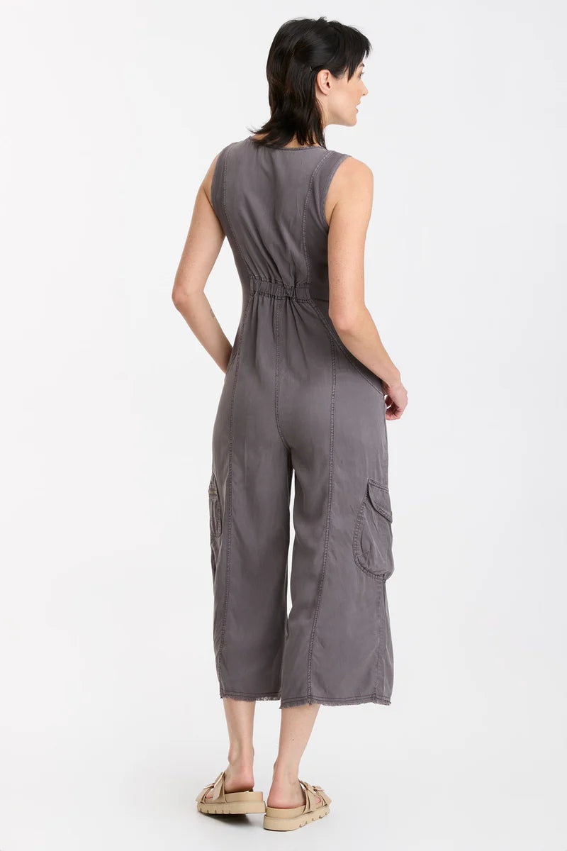 In Soft Twill, this v-neck crop jumpsuit features twill tape details throughout, plentiful pockets, antique brass hardware, a raw-edge hem, an elastic band at the center back for a contoured fit, and contrast front and back ribbed side panels for movement-friendly comfort.